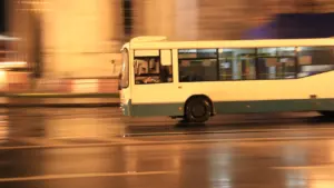 Biały autobus miejski jadący ulicą w wieczornym ruchu ulicznym w mieście.