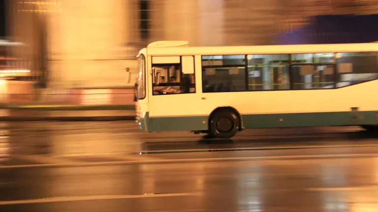Biały autobus miejski jadący ulicą w wieczornym ruchu ulicznym w mieście.