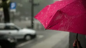Zbliżenie na różowy parasol podczas ulewnego deszczu w polskim mieście.