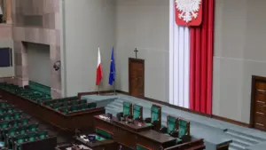 Pusta sala posiedzeń Sejmu RP z widocznym orłem w koronie na ścianie.