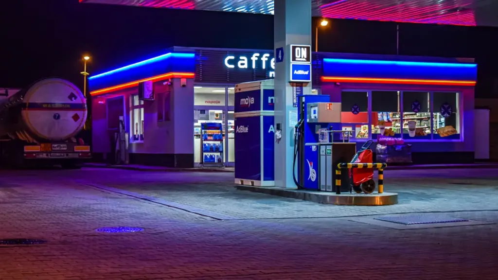 Oświetlona stacja paliw w nocy z widocznym dystrybutorem i neonowymi światłami w tle