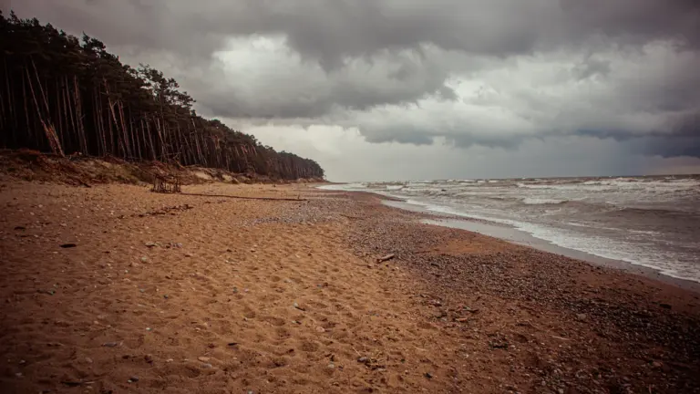 Piaszczysta plaża nad Bałtykiem pod pochmurnym, burzowym niebem, zwiastująca zmienną aurę weekendową.